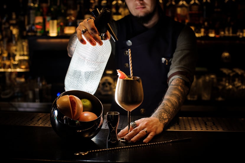 Bartender with tattoo pouring soda into the copper cocktail glass